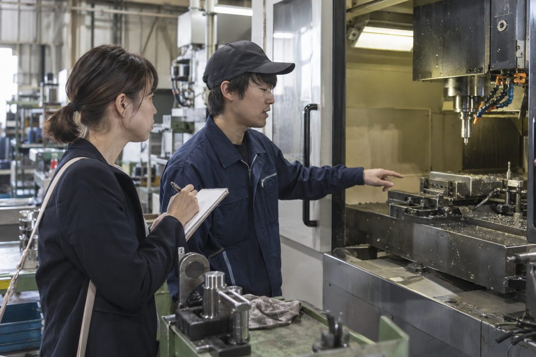 機械の前で若手社員に話を聞く担当者